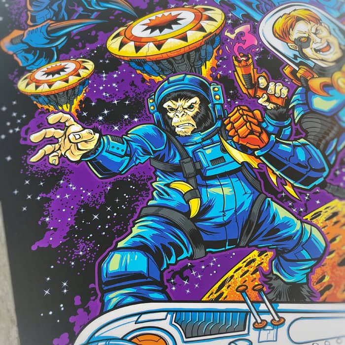 A Pinball Expo 2022 poster of a trio of space fighters (a girl, man, and chimp) working together to take down a pinball space alien.